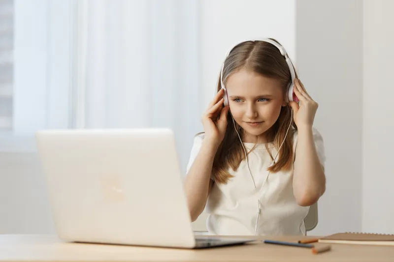 Young girl with headphones focused on online learning in a bright, modern workspace, showcasing enthusiasm for digital education