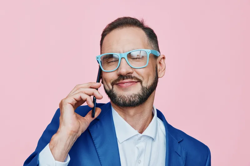A business professional man on an isolated colored background, exuding confident emotion while talking on a phone in a clean corporate setting.