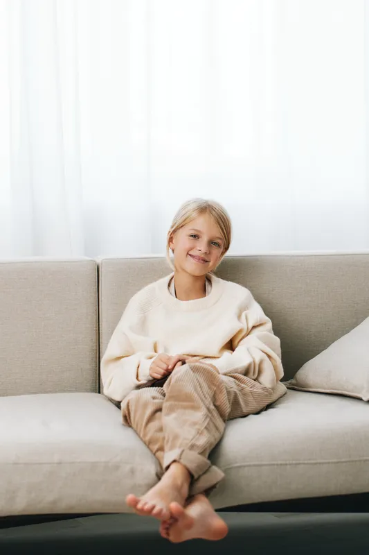 An authentic scene of a young child at home, relaxed in casual attire, embodying a warm lifestyle, soft light, and gentle play on a neutral sofa.