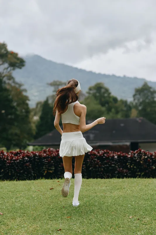 Young sporty model in white activewear running joyfully outdoors in a lush green park, showcasing a healthy lifestyle and vibrant energy