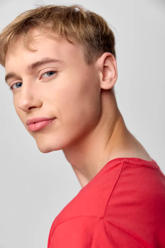 Young man in a bright red shirt turns slightly to the camera, giving a confident gaze in a clean studio setting, with soft lighting and a casual, expressive mood for stock use