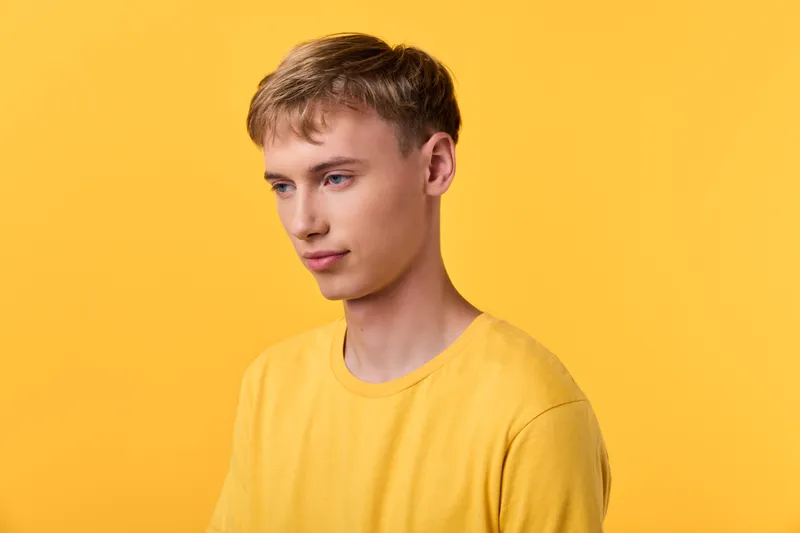 Young man in a yellow shirt stands before a bright studio backdrop, casual fashion vibe with a relaxed pose, soft lighting and minimal setup for a clean lifestyle image suitable for ecommerce and