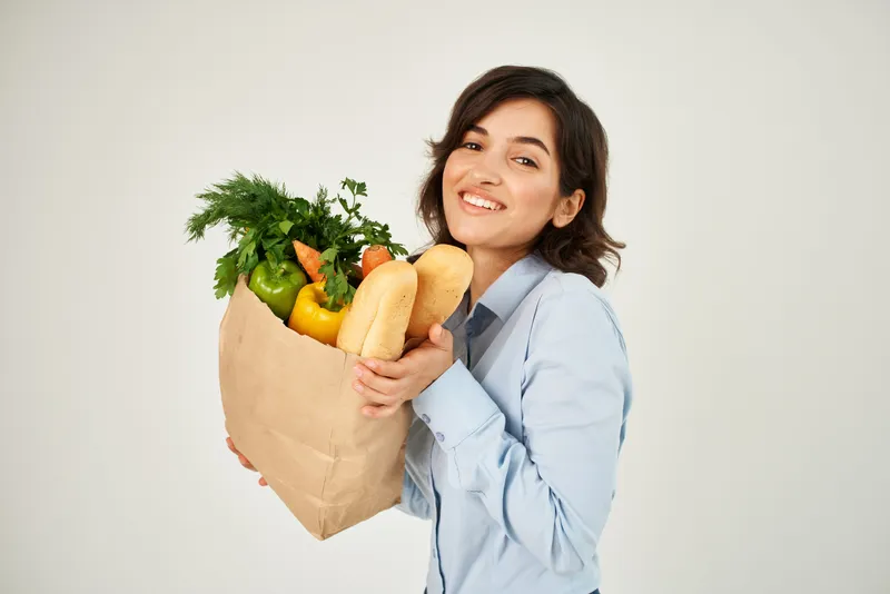 Веселая женщина с пакетом продуктов из супермаркета покупает овощи