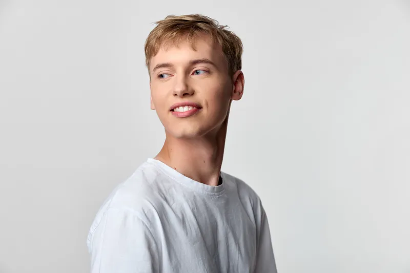 Smiling man in a white t shirt looks to the side in a clean studio setting, conveying ease, confidence, and approachable charm for lifestyle or fashion concepts.