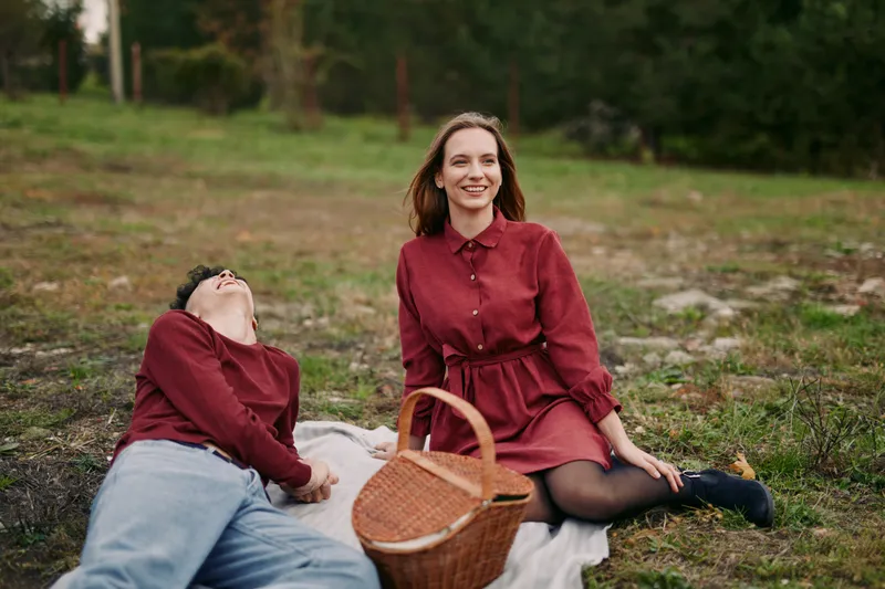 A picnic portrait of two friends sitting on a blanket in a meadow, authentic candid interaction with genuine smiles and relaxed posture conveying credibility and natural warmth.