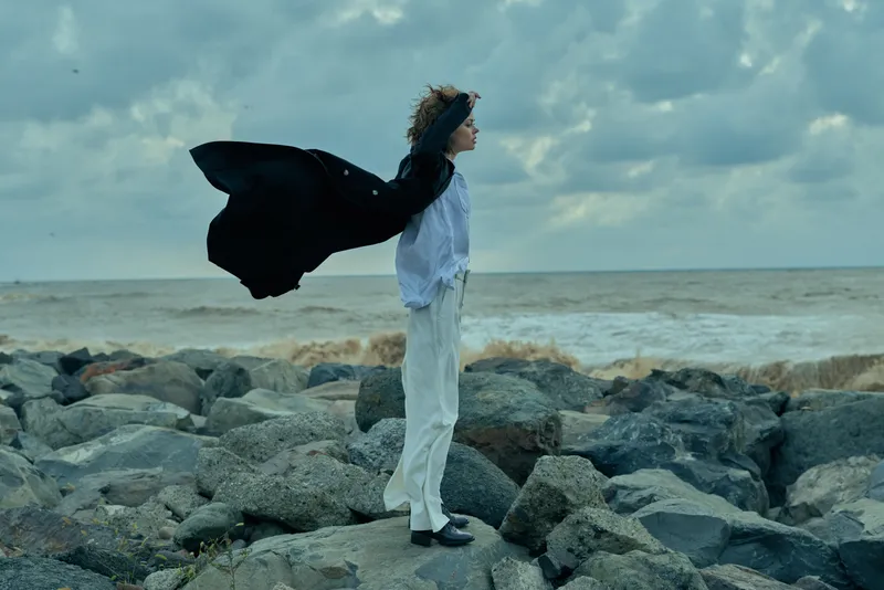 woman cape wind sea rocks outdoor drama freedom fashion motion silhouette coastline horizon dramatic wind swept moment on rocky shore