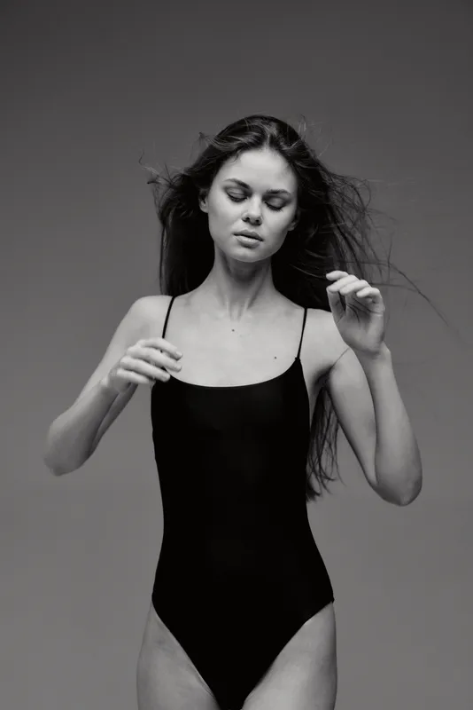 black and white woman posing in black swimsuit with flowing hair and closed eyes