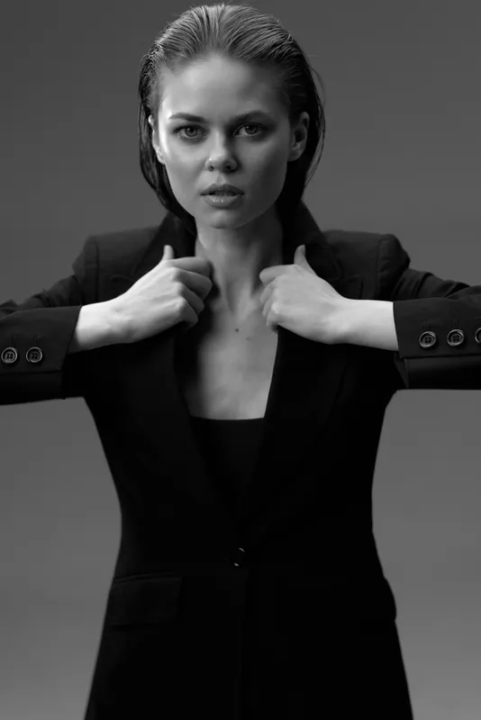 Black and white portrait of a confident woman wearing a blazer in a studio setting with an intense gaze.