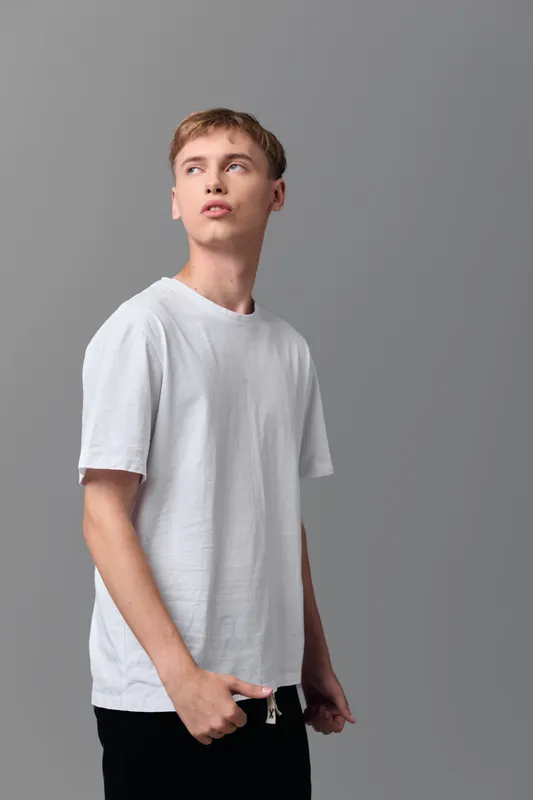 Young man in white tshirt gazing off to the side against a neutral gray backdrop, casual street style, clean wardrobe, minimal setup, suitable for lifestyle and fashion imagery