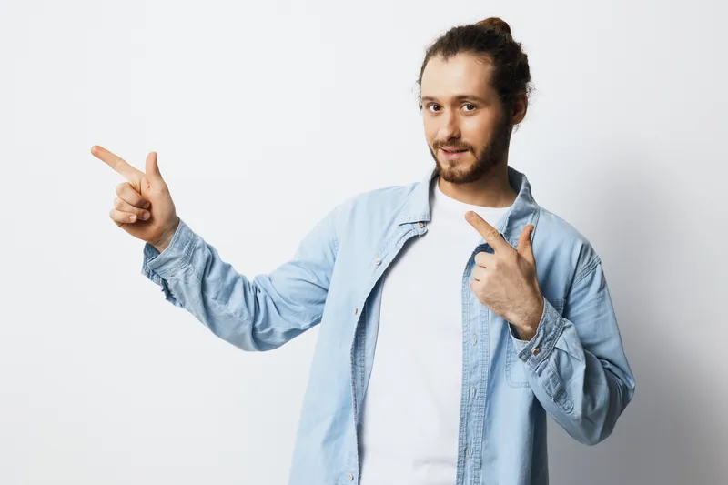 Young man in denim shirt showcasing enthusiasm and joy, gesturing with fingers against a neutral background, ideal for marketing and lifestyle themes