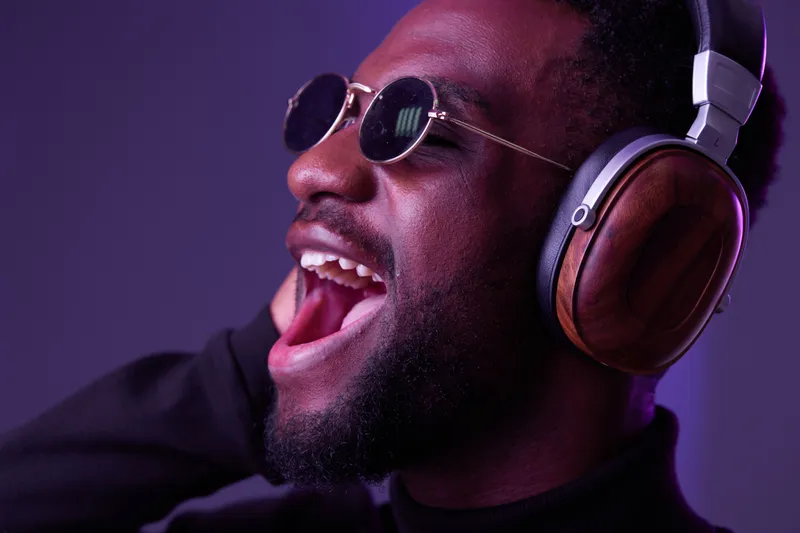 Happy Black man singing with headphones, expressing joy in a colorful studio setting with vibrant purple lighting and stylish sunglasses