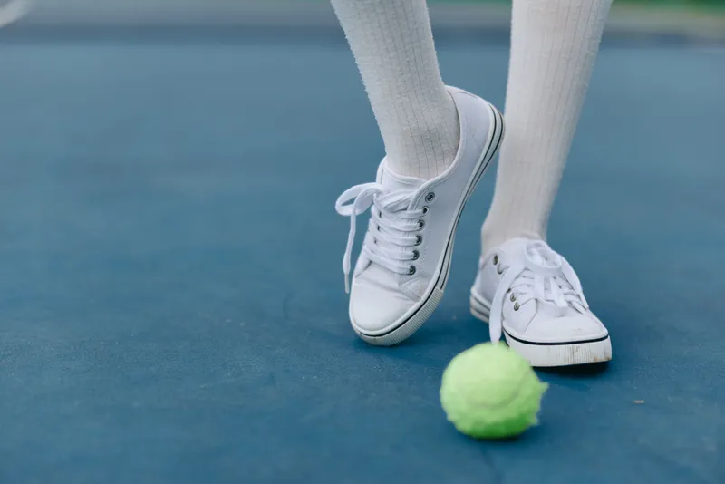 Female athlete in white sneakers playing tennis, showing focus and determination on a blue court with a tennis ball