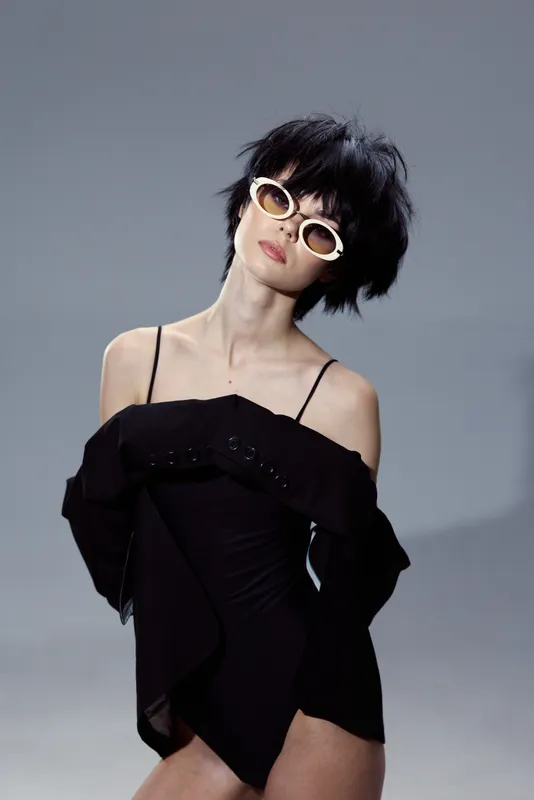 Woman wearing black dress and sunglasses posing with short hair against gray background