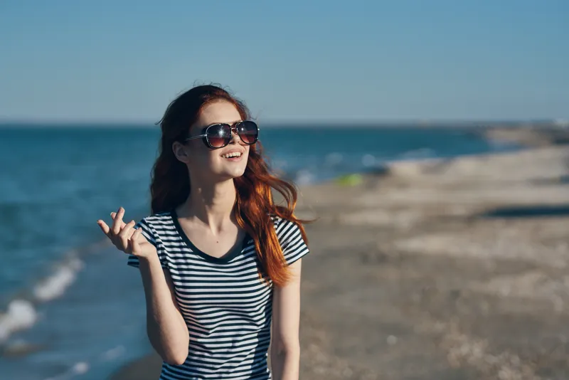 Портрет женщины в футболке и очках на пляже в горах у моря