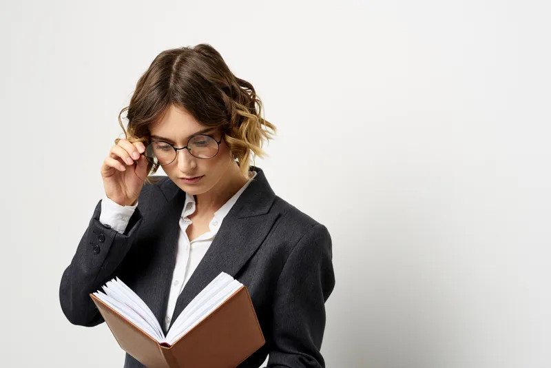 Женщина на работе с книгой в руке, светлый фон, классический костюм, очки, голова