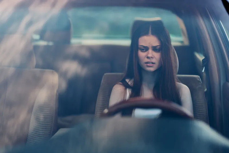 Young woman sitting in a car, looking stressed while checking her phone, conveying emotions of worry and uncertainty in a candid moment.