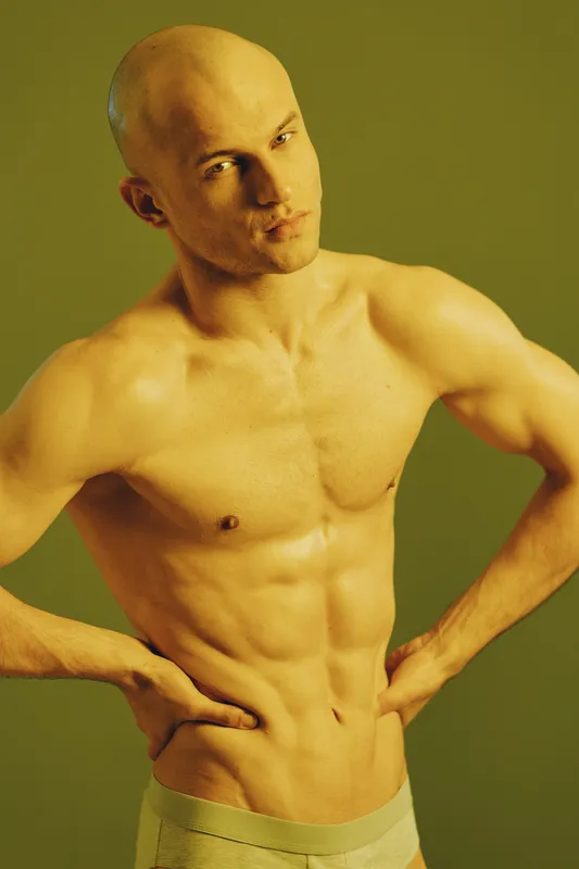 Focused man posing with confidence, showcasing a toned physique. The image features a subtle yellow-green background, emphasizing strength and determination.