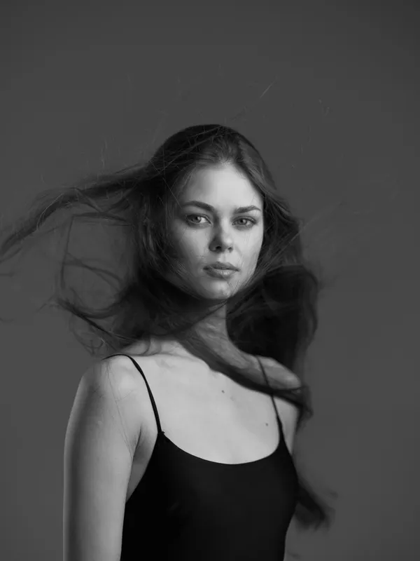 Black and white portrait of a young woman with flowing hair wearing a black dress on a gray background.