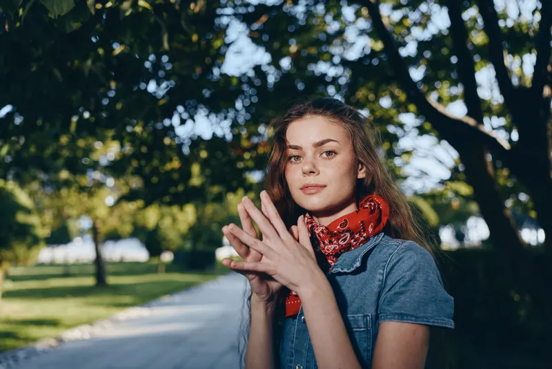 Lifestyle woman in modern boho-western denim street style with red bandana, casual pose outdoors, natural light with film color effect, relaxed summer vibe.