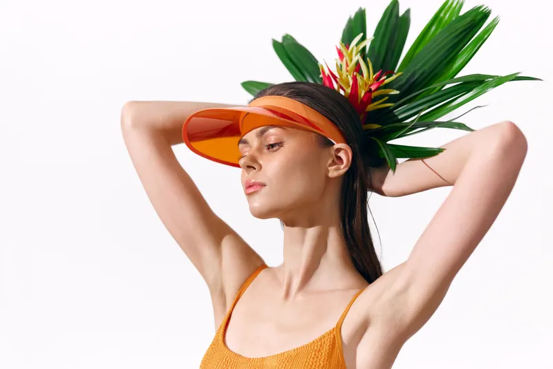 Стильная женщина в оранжевом купальнике и козырьке с тропическими цветами, излучающая уверенность и летнее настроение, идеально подходит для модных тем и тем образа жизни