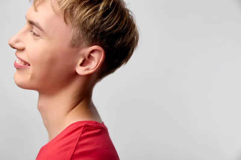 Smile, side profile of a cheerful young male in a red shirt, bright studio lighting and simple background, conveying positive mood and friendly casual style