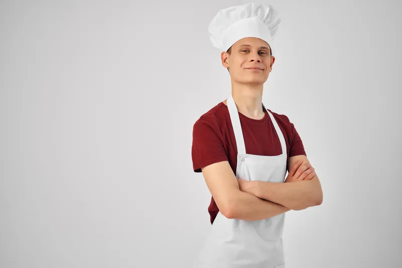Мужчина-повар в фартуке и колпаке на голове на светлом фоне