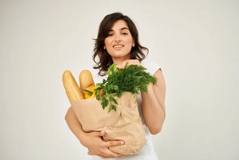 Весёлая домохозяйка с пакетом продуктов из супермаркета, ассоциирующихся со здоровой пищей
