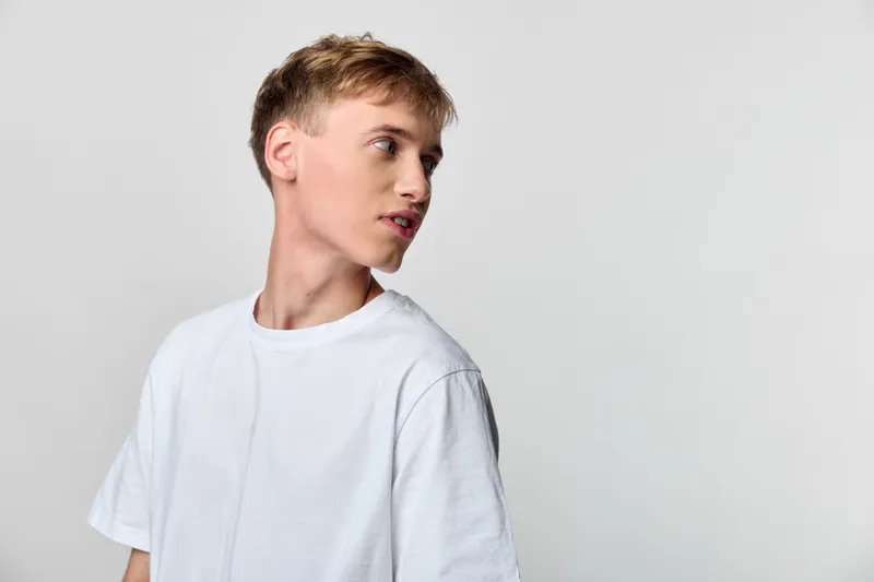 Youthful male in a tshirt looks away in a studio shot, conveying casual fashion, neutral background, calm expression and minimal clean style for commercial use