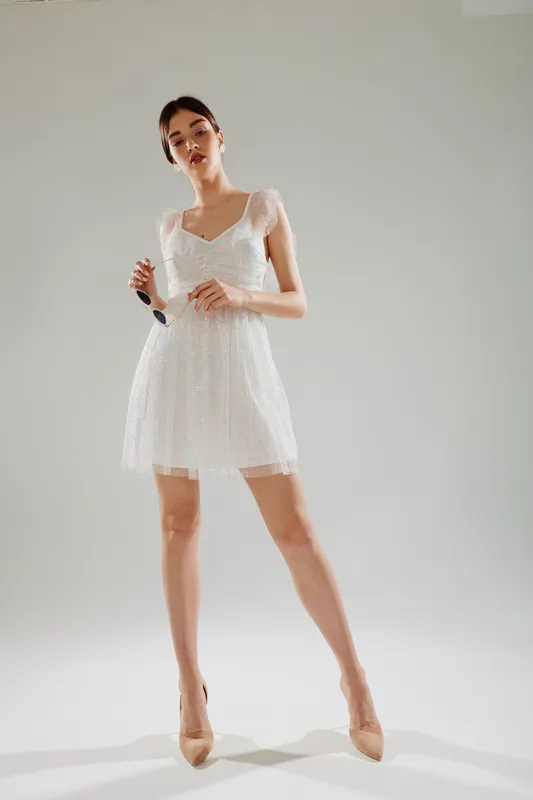 Young woman in a white lace dress posing in a studio with a neutral background. Concept for beauty, fashion, elegance, and modern style.