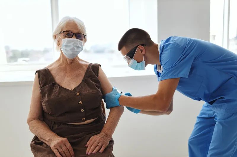Врач-мужчина делает пожилой женщине инъекцию вакцины от COVID-19 в больнице