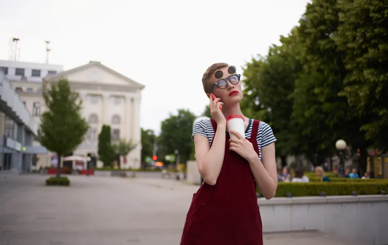 Женщина с напитком в чашке, в очках, гуляет на свежем воздухе на улице
