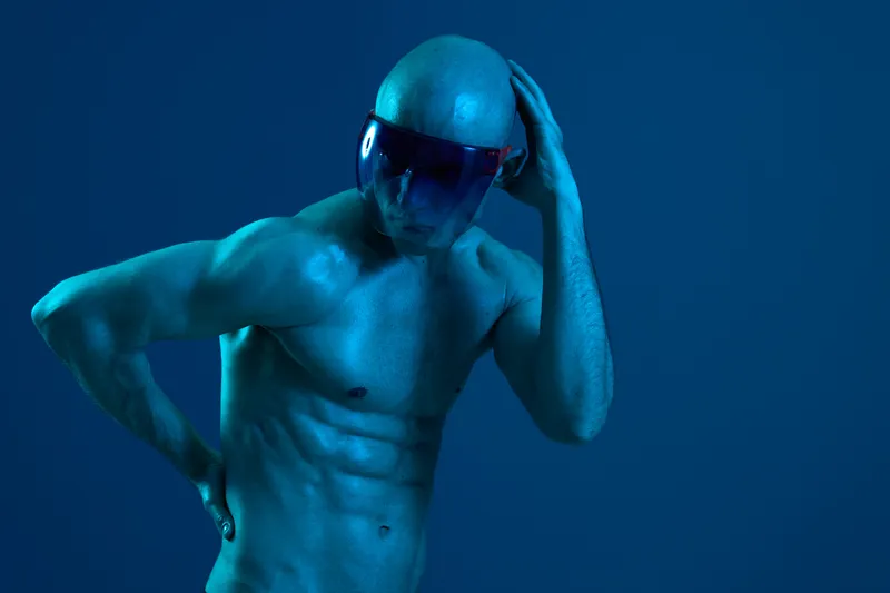 Athletic man with a futuristic visor poses against a blue background, showcasing a modern and dynamic feel. The image highlights strength and style in a striking manner.