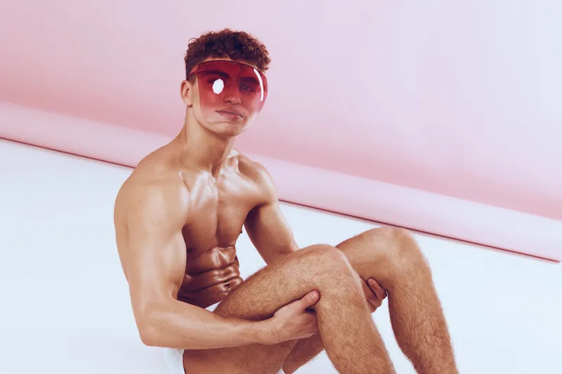 Мускулистый молодой человек с вьющимися волосами излучает уверенность, сидя в расслабленной позе