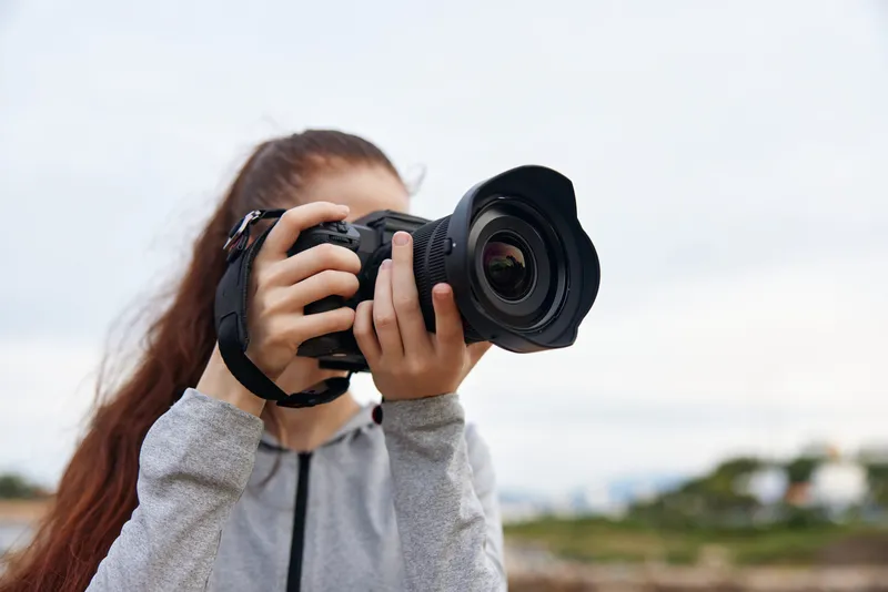 Young woman in casual clothing passionately holding a camera outdoors, capturing breathtaking landscapes, showcasing her love for photography and nature