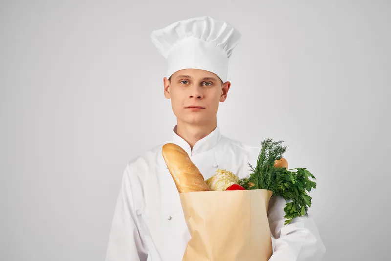 Мужчина в одежде повара с упаковкой продуктов занимается приготовлением еды на кухне