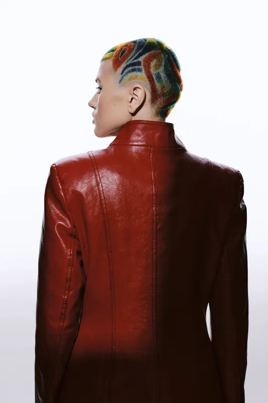 woman with colorful shaved hair wearing a glossy red leather jacket, modern fashion style, bold look, creative hairstyle, edgy clothing, studio portrait with white background