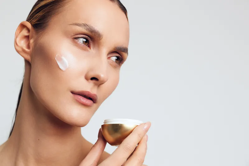 Woman skincare routine, cream near the eye, beauty face hydration, holding a small cup, selfcare and spa care, soft studio light for tired skin