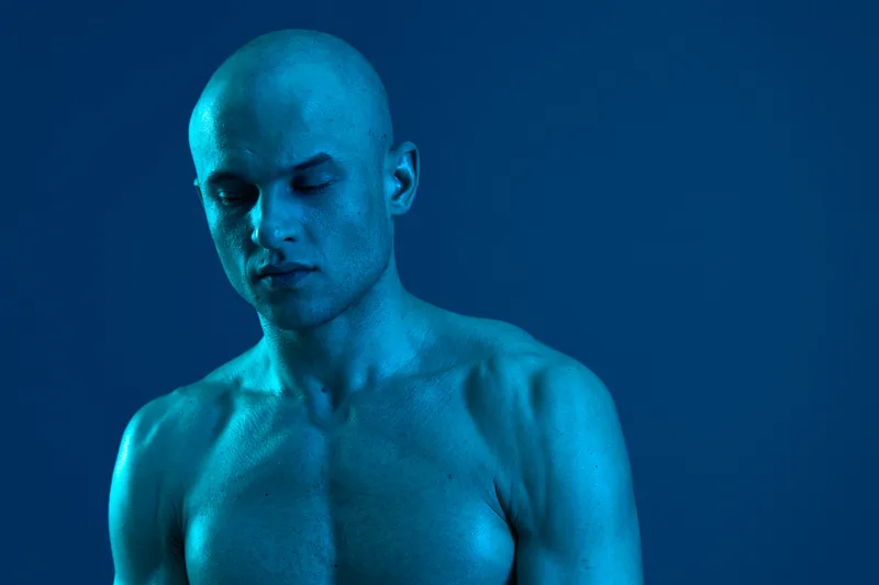 A contemplative man in a striking blue hue, showcasing strong features and emotive expression, surrounded by a minimalist blue background, emphasizing depth and introspection.