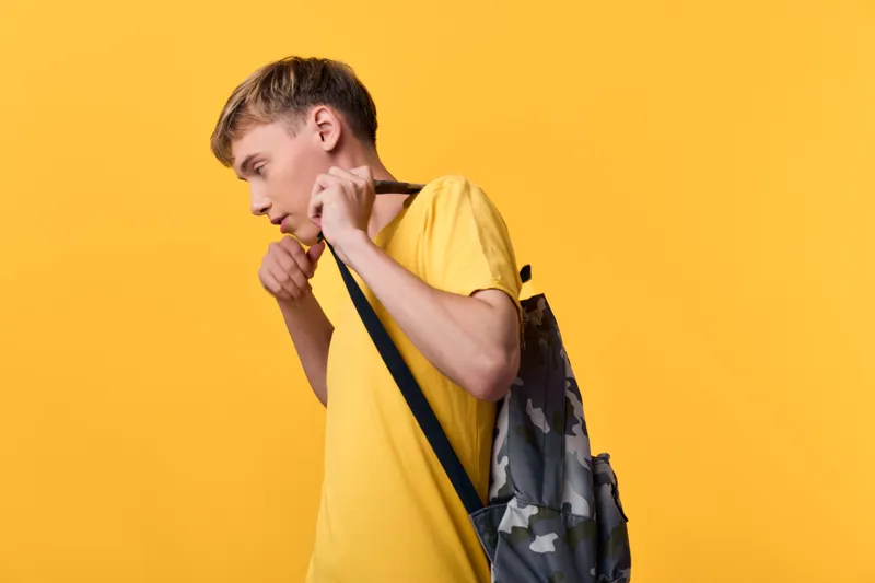 Backpack on shoulder, student adjusts strap against a bright yellow backdrop, casual style, daily commute and education themed scene, urban lifestyle and focus