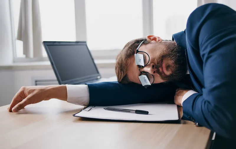Бизнесмен в костюме уснул за работой за столом в офисе