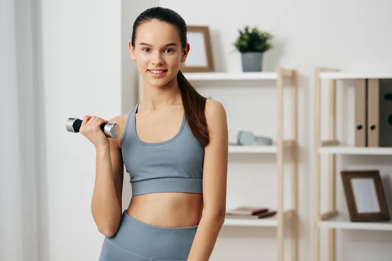 Fitness woman in athletic wear lifts a dumbbell indoors, showcasing strength, focus, and motivation for a workout, training, and healthy lifestyle in a modern home setting.