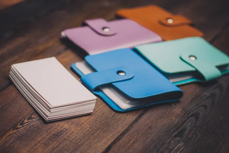 Яркие держатели для визиток и пачка белой бумаги на деревянном фоне, крупный план