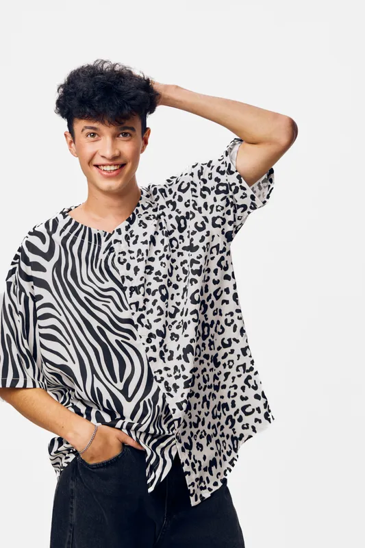 young man wearing black and white animal print shirt smiling confidently with hand on head, casual style against plain light background, cheerful and relaxed mood