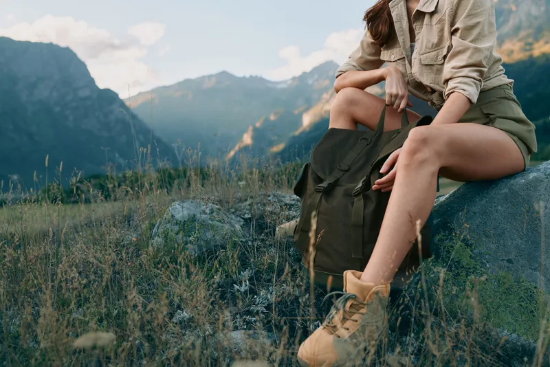 Woman lifestyle traveler sitting on a rock in the mountains wearing hiking boots and casual clothes, enjoying nature and outdoor adventure in a scenic landscape.