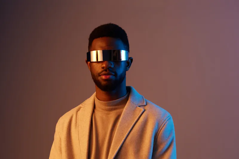 Stylish young man wearing futuristic sunglasses in a modern outfit, showcasing confidence against a vibrant gradient background