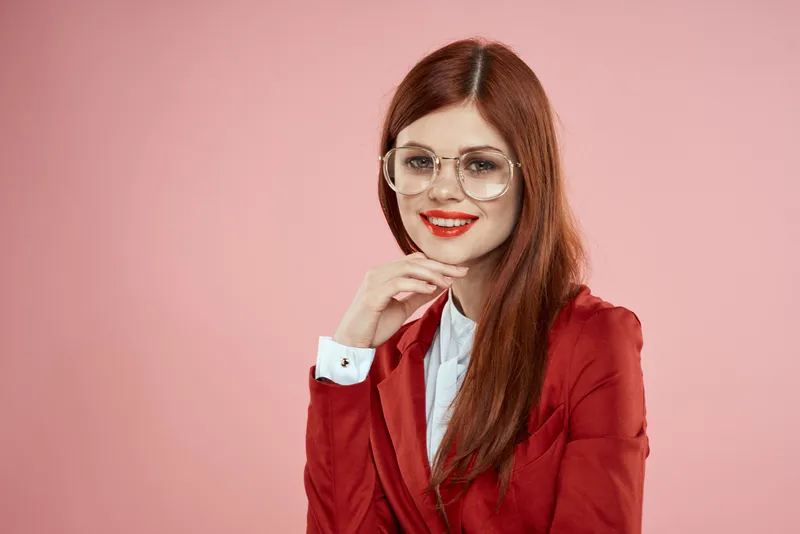 Женщина в красном пиджаке, в очках, с красными губами и длинными волосами на розовом фоне