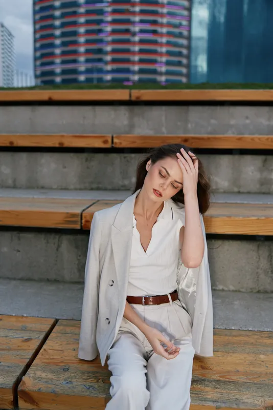 Businesswoman in a modern urban setting, dressed in a light grey blazer and trousers, conveying a sense of focus and determination while seated on wooden steps.