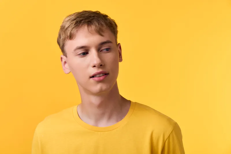 Young man in a bright yellow shirt stands against a solid yellow background, creating a bold monochrome look ideal for fashion, studio, lifestyle, or product presentation.
