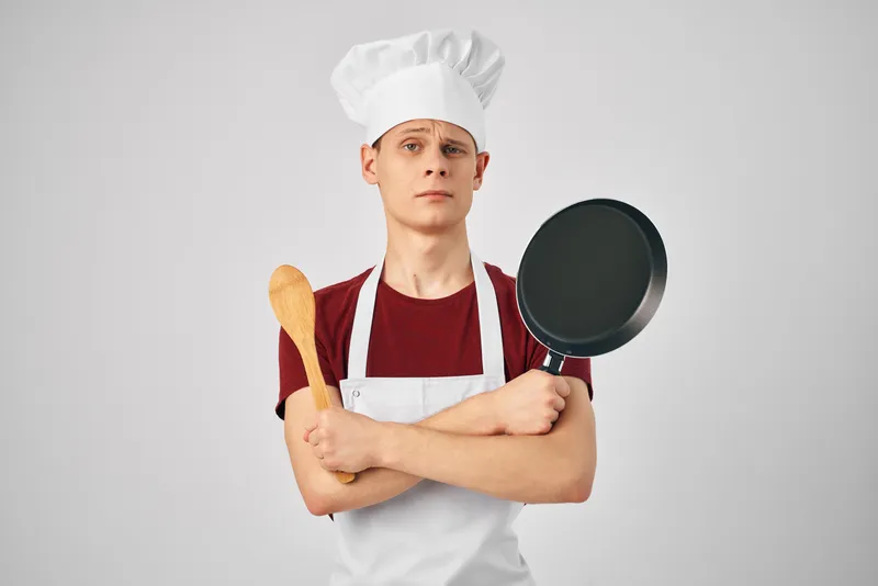 Повар в форме с кухонной утварью профессионально занимается приготовлением пищи
