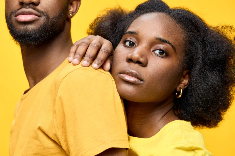A close up of a young Black couple dressed in bright yellow clothing, showcasing emotions of love and intimacy against a vibrant yellow background